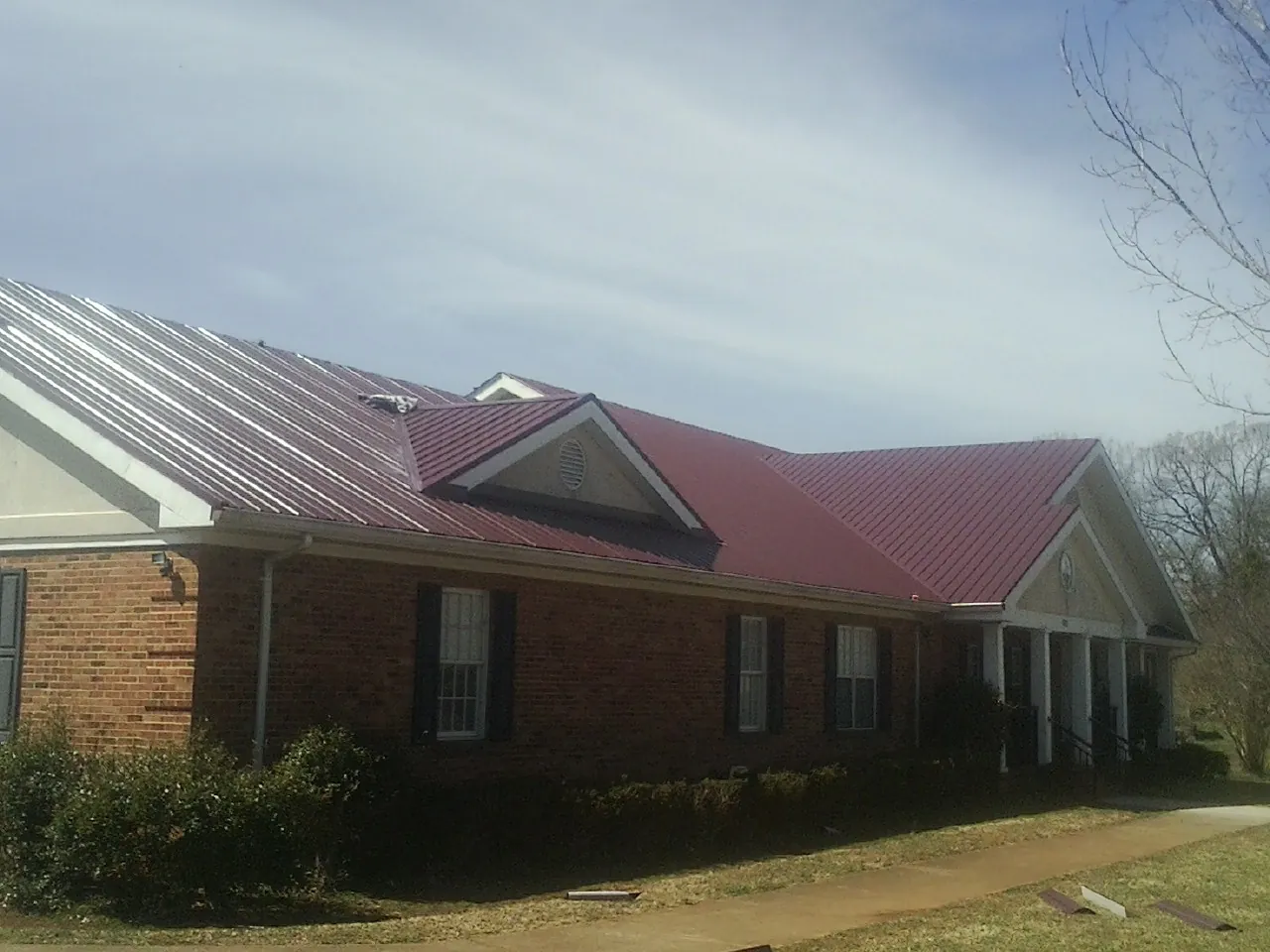 Red metal roof with gabled entries on a long brick building, from a Hail Damage Roof Repair job in Hastings