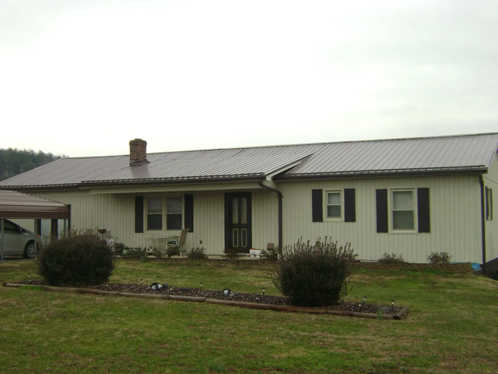 Brown metal roof on a cream sided ranch home with a brick chimney in Hastings